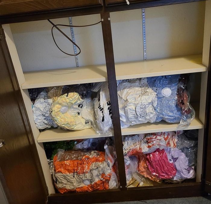 A cabinet neatly organized with shelves, filled with compressed bags of vibrant bedding and clothing items