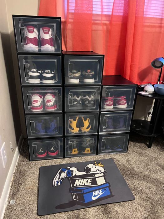 A display showcasing different Nike sneakers stored in transparent boxes, with a Snoopy-themed Nike mat placed on the floor beneath.