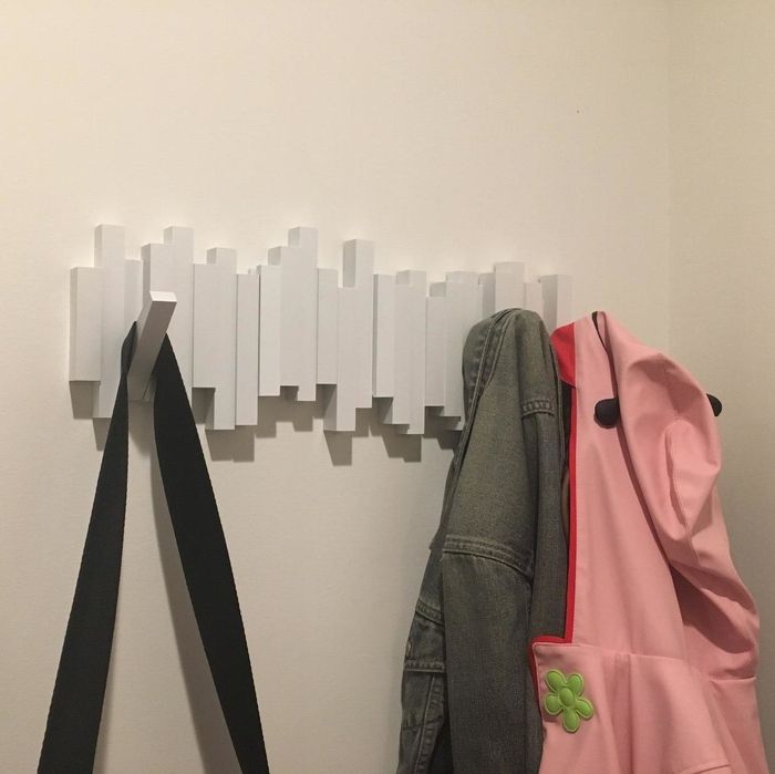 a reviewer's photo of a white wall-mounted hook unit with two coats and a bag hanging from it