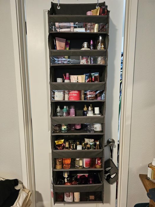 Hanging organizer on a door, filled with an assortment of beauty products such as lotions, perfumes, and skincare items, all neatly arranged in individual compartments
