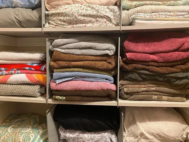 A photo from a reviewer showing shelf dividers in action, neatly separating stacks of towels inside a linen closet.