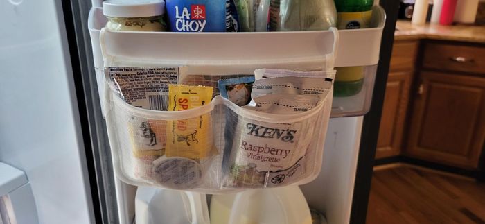 Refrigerator door with condiment packets, including Ken's Raspberry Vinaigrette, neatly organized in a mesh holder, next to a carton of milk