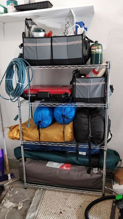 A durable metal shelf in a garage, neatly arranged with bins, a hose, and camping equipment