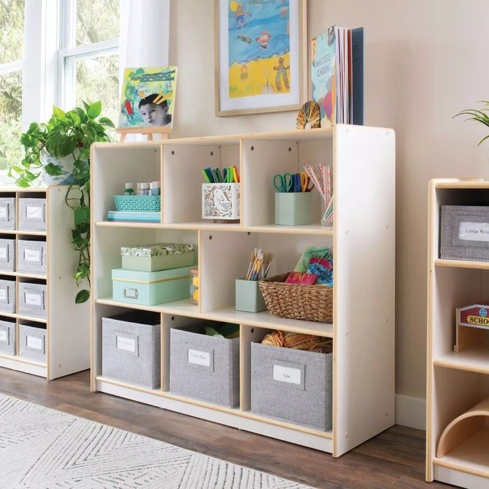 A room with neatly arranged shelves filled with labeled boxes, baskets, plants, and children’s books, perfect for both home and classroom storage.