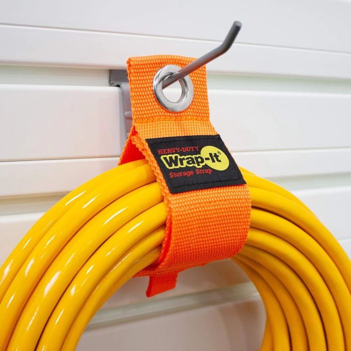 A heavy-duty Wrap-It storage strap holding a coiled yellow hose on a metal hook attached to a wall panel
