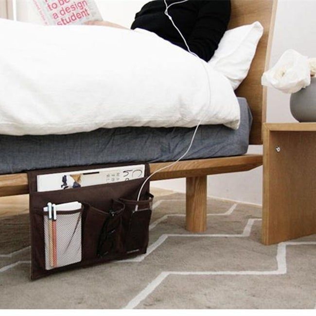 A bed with a bedside caddy hanging from the bed frame, holding essential items like a phone, glasses, and a magazine.