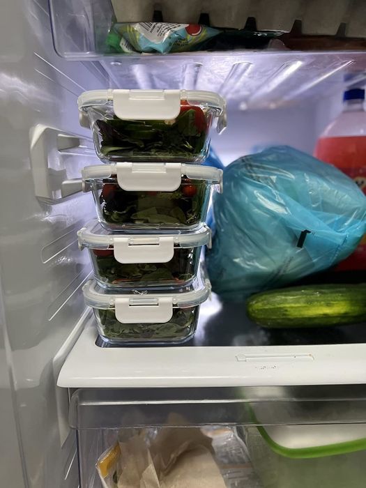 Transparent food storage containers stacked and filled with fresh greens, stored inside a refrigerator