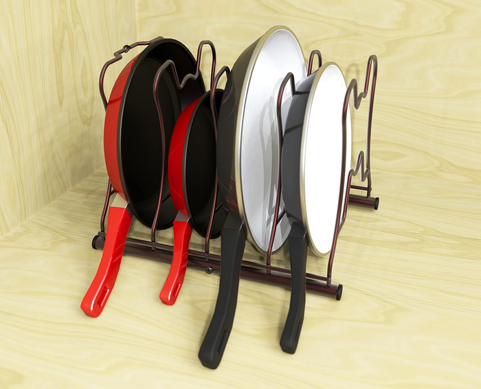 Five frying pans of various sizes are neatly arranged in a wooden rack with curved sections to hold each pan securely.