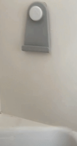 A gif of a reviewer scooping bath toys out of the water and hanging the storage bag on the wall.