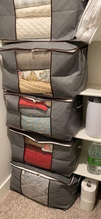reviewer's stacked storage bags filled with blankets and linens, organized on shelves alongside cleaning supplies in the closet