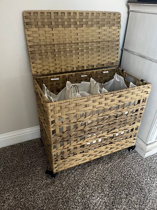 Woven laundry hamper with a hinged lid, lined with fabric interior bags, resting on a carpeted floor