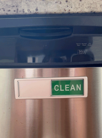 A person toggling the dishwasher magnet to indicate the dish status.