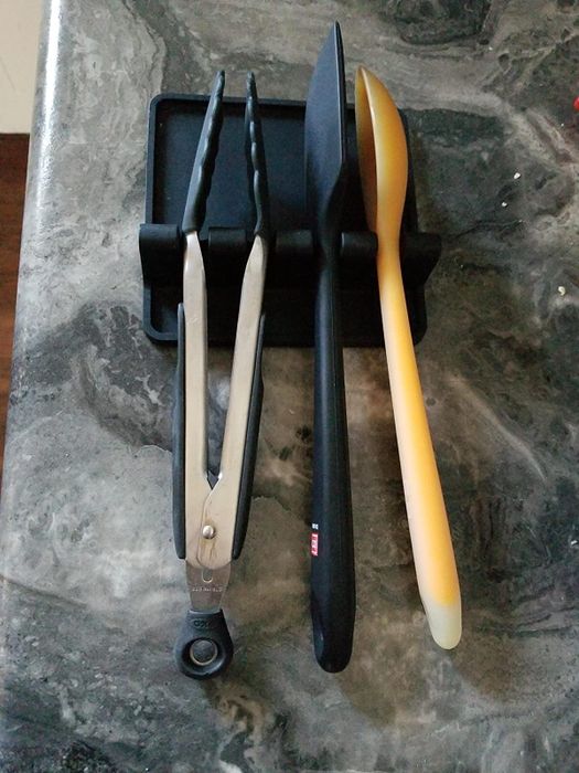 A reviewer's utensil rest holding tongs, a serving spoon, and a spatula.