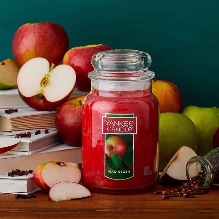 a large red candle in a glass jar featuring an apple on the label