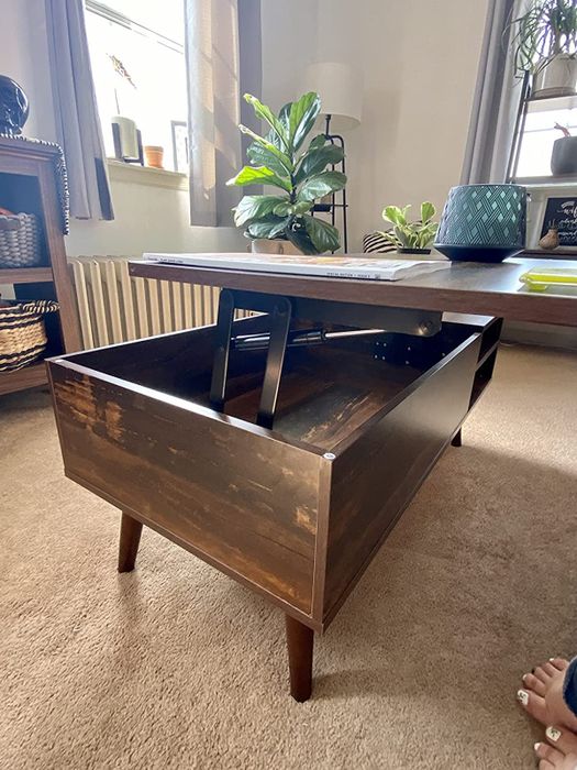 A reviewer's photo of the coffee table with its top in the lifted position, showcasing its dual functionality as a workspace and storage unit.