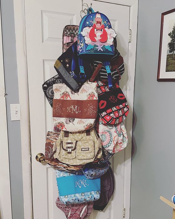 A collection of backpacks and handbags hanging on a door, featuring an array of patterns and styles for easy access and display.