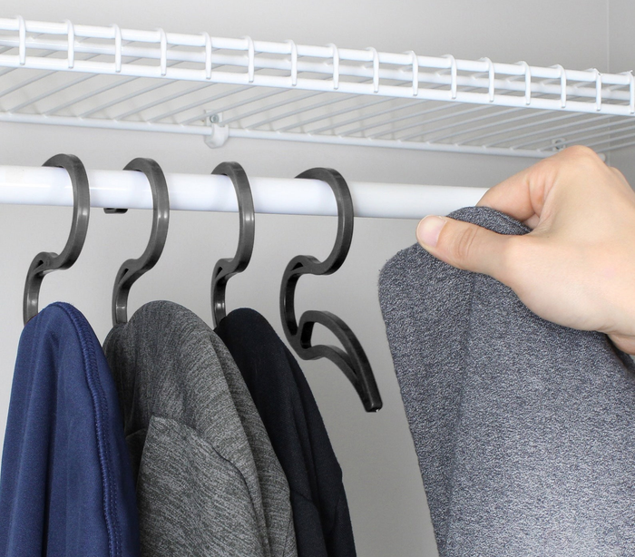 four black hoodie hangers in a closet with a person’s hand pulling one out