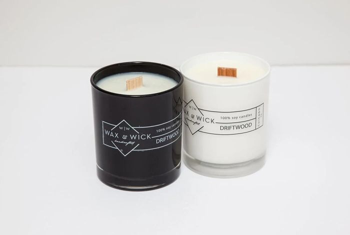 a black candle placed next to a minimalist white design, alongside a white candle with black accents, both featuring thick wooden wicks