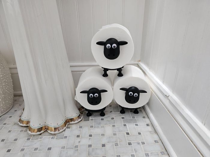 Toilet paper rolls featuring sheep faces stacked on a bathroom floor