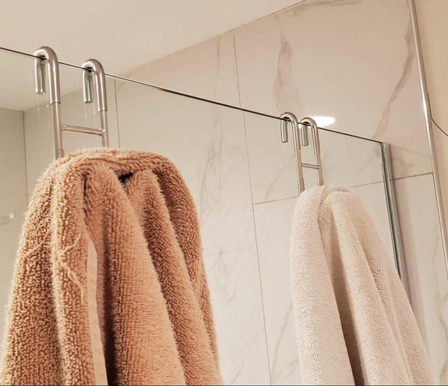 Two towels neatly hung on a glass shower door using sleek stainless steel s-shaped hooks.
