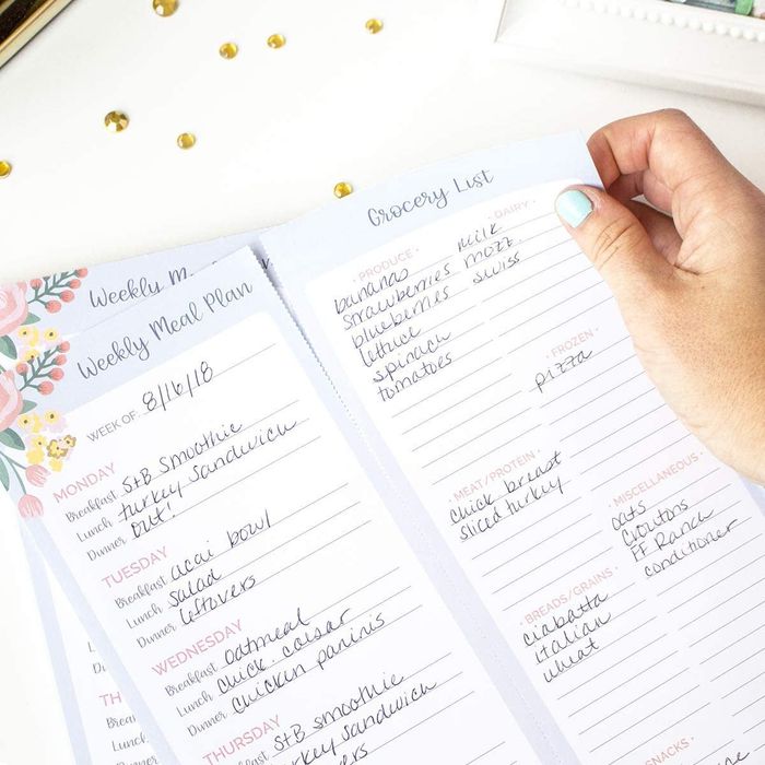 A model holding a meal planning pad, tearing off the grocery list.