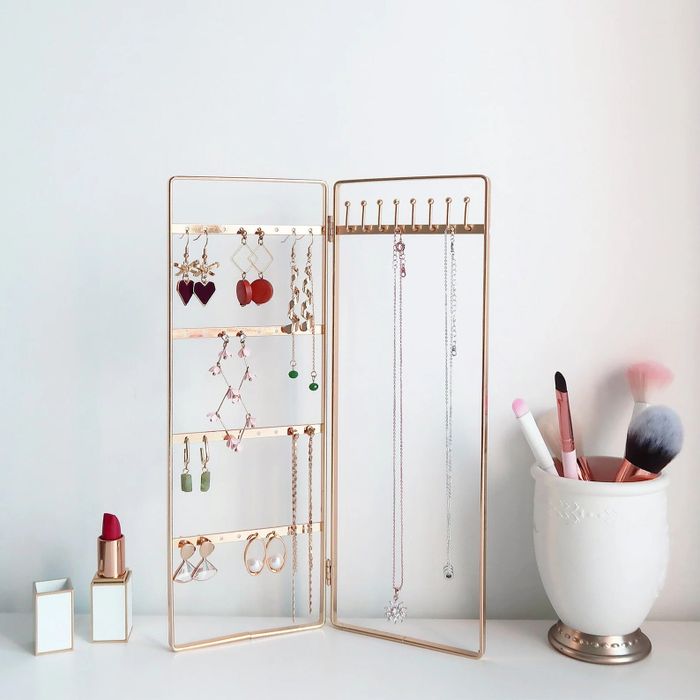 The elegant gold bi-folding jewelry stand on a counter, with various baubles hanging from it