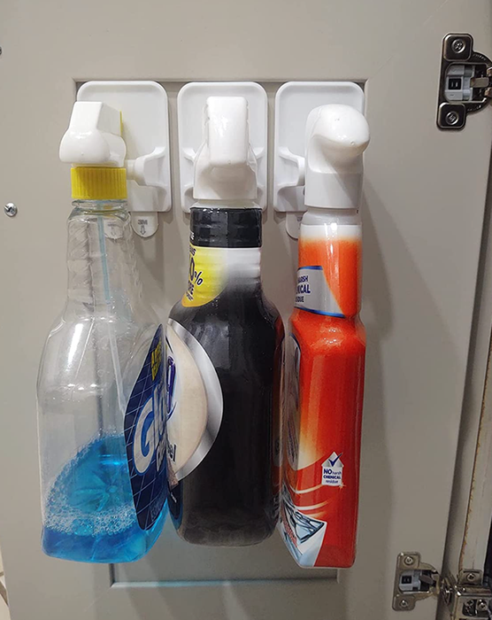 Three bottles hanging on white Command hooks inside a cabinet.