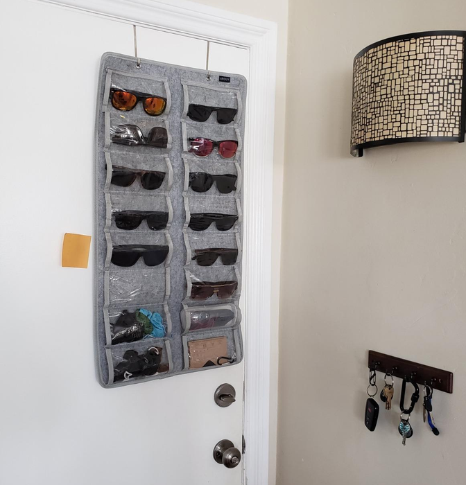 A reviewer's gray sunglasses organizer hanging on the door from two metal hooks