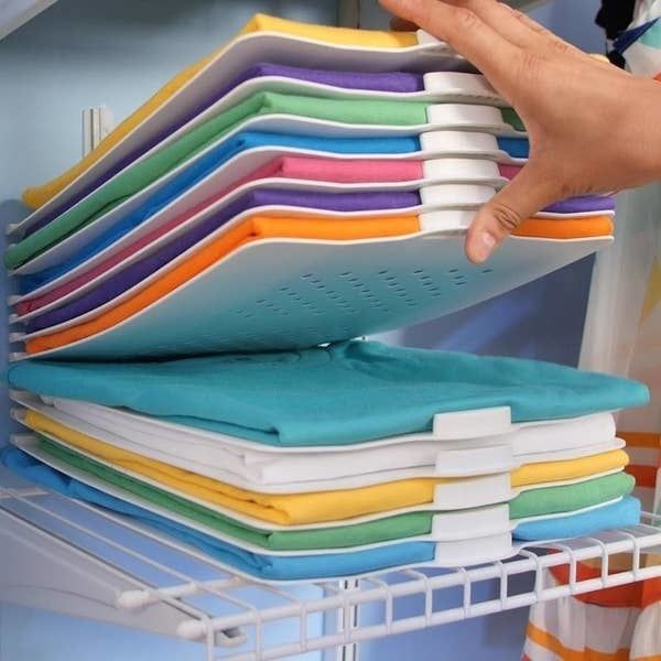 A hand holds up brightly colored T-shirts, all neatly folded and stacked using the white EZSTAX organizer.