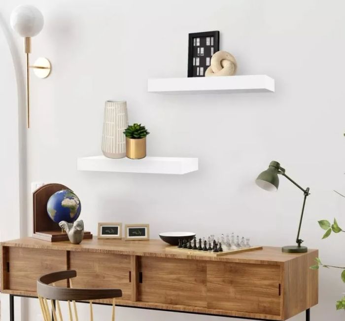 A modern, minimalist home office with a wooden desk, shelves showcasing small decor, a globe, a lamp, and a chess set