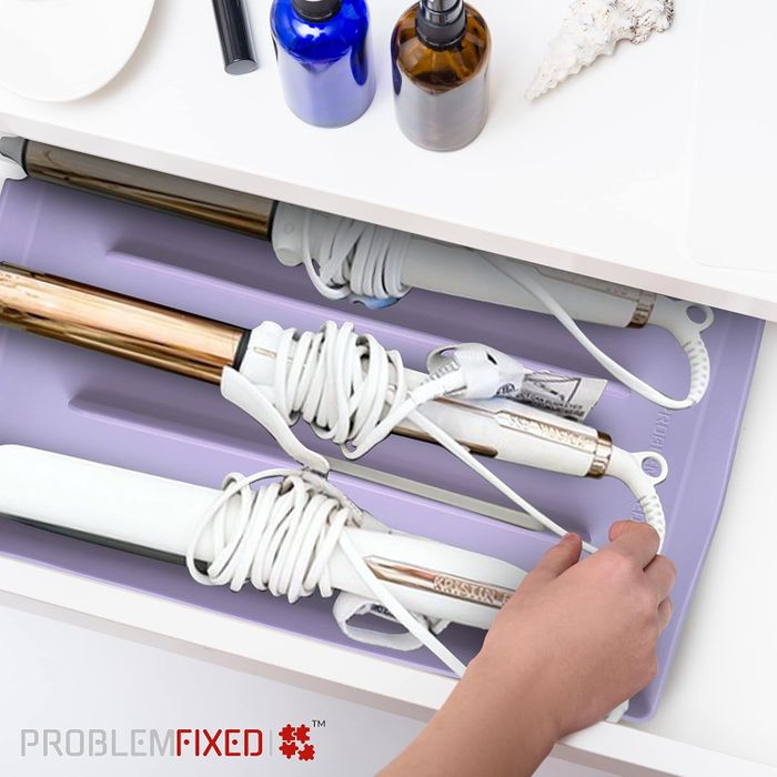 A person neatly arranges styling tools in a drawer using a silicone mat that keeps cords from tangling. The image is from the brand Problem Fixed® and shows an organized array of styling devices