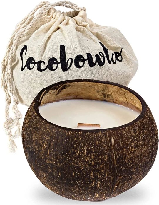 A candle made from a coconut shell placed beside a canvas pouch