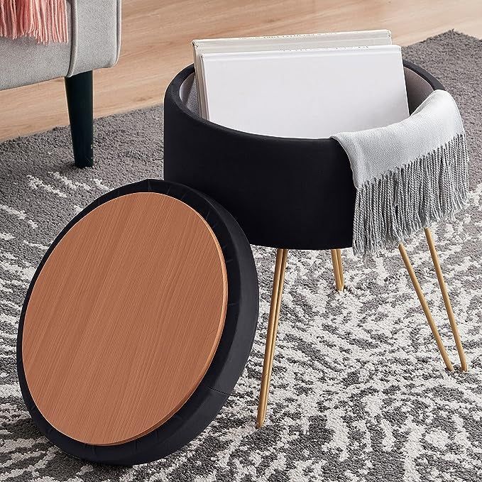 A sleek black side table featuring a round wooden top and a black storage compartment, supported by three brass legs