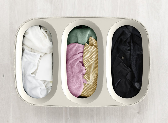 A three-section laundry hamper, with clothes sorted into white, colorful, and dark categories.