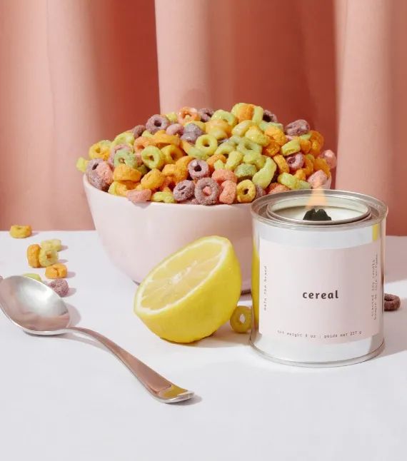 Candle lit with a wood wick, placed in front of a bowl of cereal