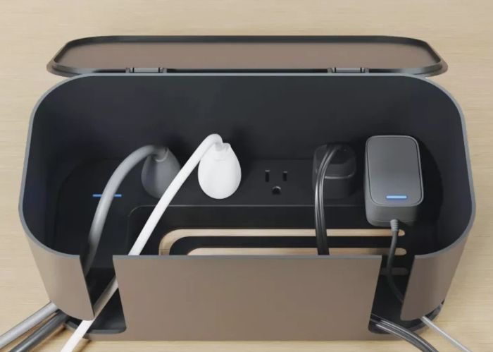A cable management box neatly arranging cords plugged into a power strip with three outlets, highlighting its effectiveness in decluttering and organizing cables