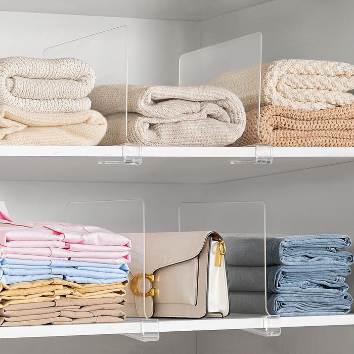Closet shelves with neatly arranged folded clothes, each section clearly divided by transparent dividers.