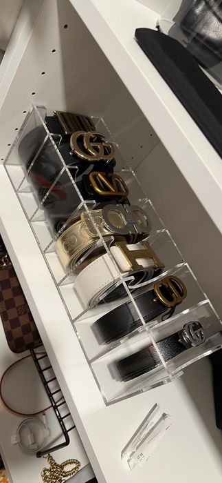 A display of designer belts, elegantly arranged in a transparent storage unit on a shelf, showcasing buckles branded with Gucci logos