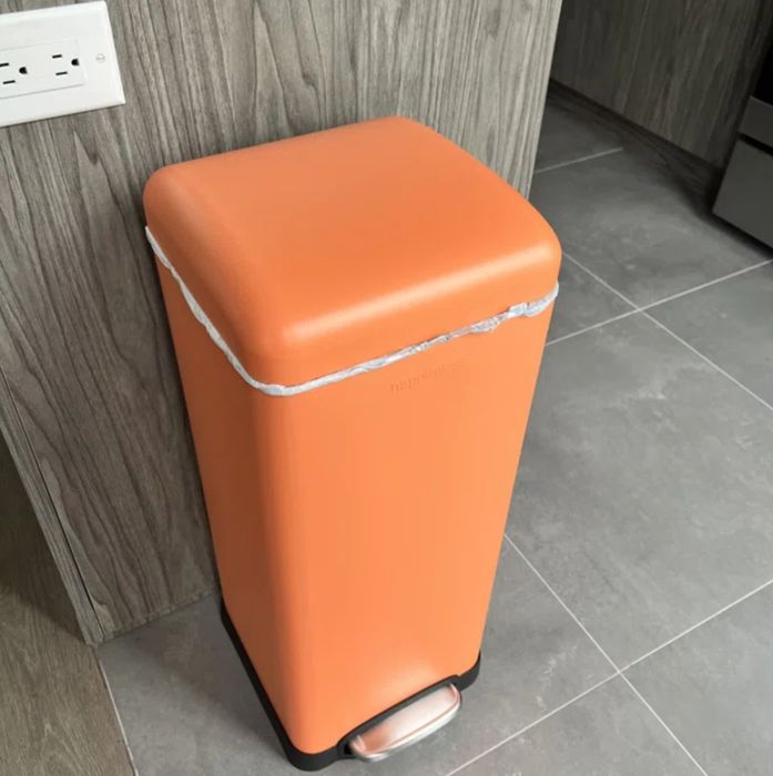 A modern orange rectangular trash bin with a foot pedal, placed in a contemporary kitchen