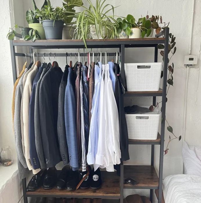 A standalone closet with shirts, shoes, bins, and plants arranged inside.