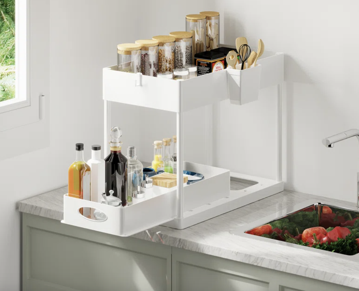 A kitchen counter displaying a white, multi-level organizer holding spice jars, bottles, and cooking utensils.