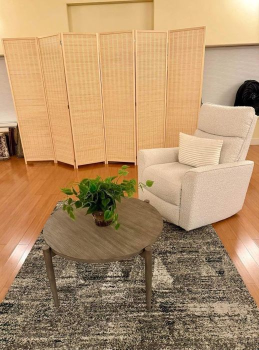 A cozy living area featuring an armchair, a round table with a plant, and a six-panel divider