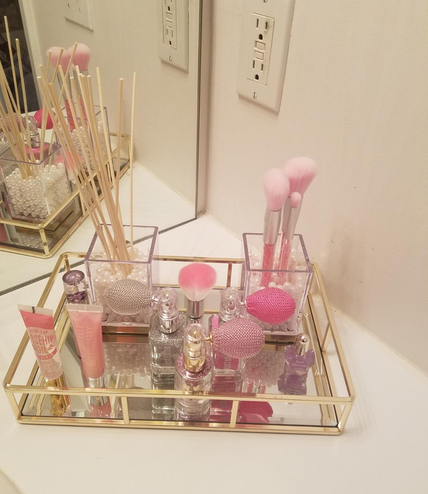 A reviewer’s photo of a mirrored and gold-trimmed tray with pink cosmetic bottles on it.