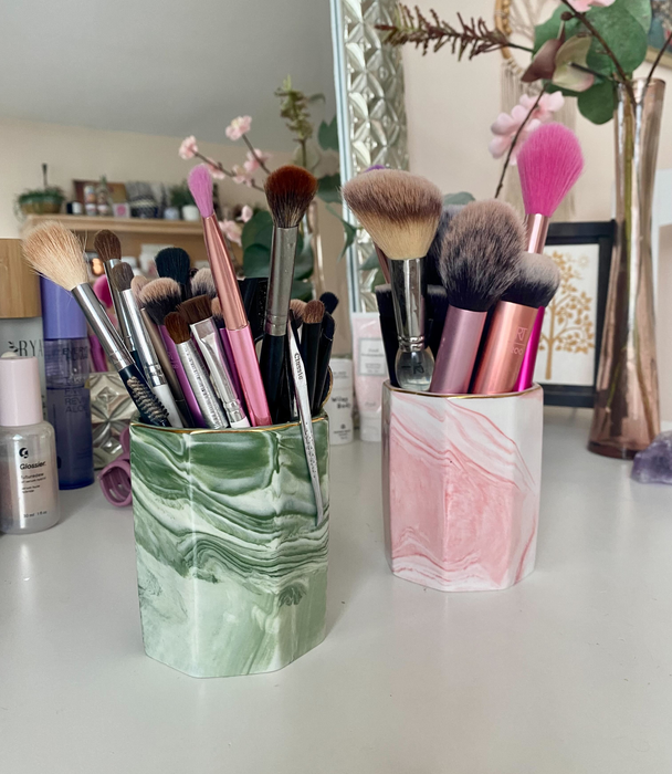 Two marble cups in green and pink filled with makeup brushes on a desk.