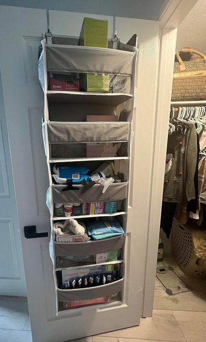 An over-the-door organizer with multiple pockets, neatly holding a variety of household and toiletry items, suspended on the back of a white door