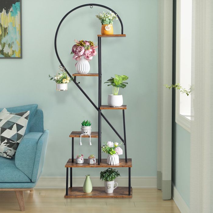 A spiral staircase-style shelving unit adorned with various plants and vases, placed in a living room