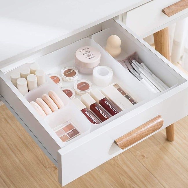 A five-compartment drawer organizer holding makeup items in a tidy white desk drawer.