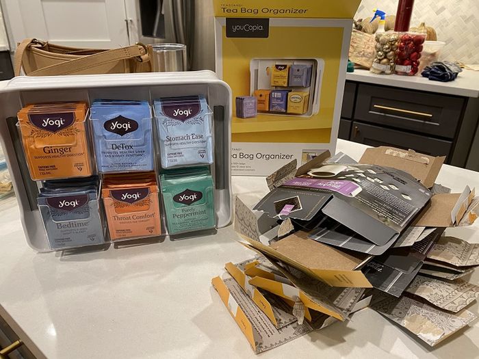 A reviewer shows the tea bag organizer placed next to a stack of flattened tea boxes, demonstrating how much space it saves.