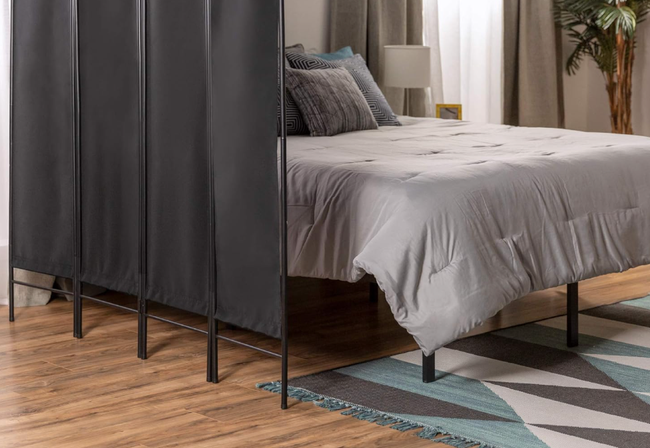 A modern bedroom setup with a gray comforter, accent pillows, and a chic room divider on a sleek wooden floor
