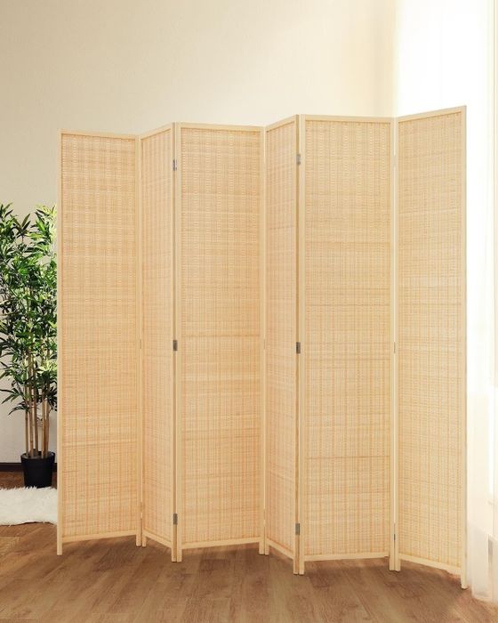 A minimalist six-panel wooden room divider placed on a hardwood floor, with a potted plant visible in the background